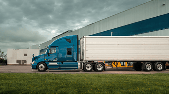 Blue semi truck parked outside a warehouse under a cloudy sky